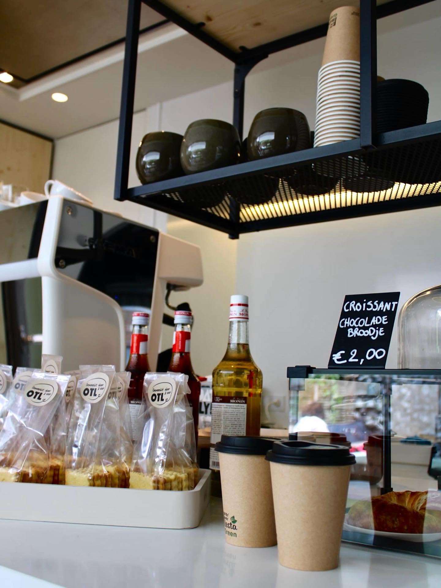 Toonbank met papieren koffiebekers, brownies in zakjes met OTL-sticker en krokante croissants