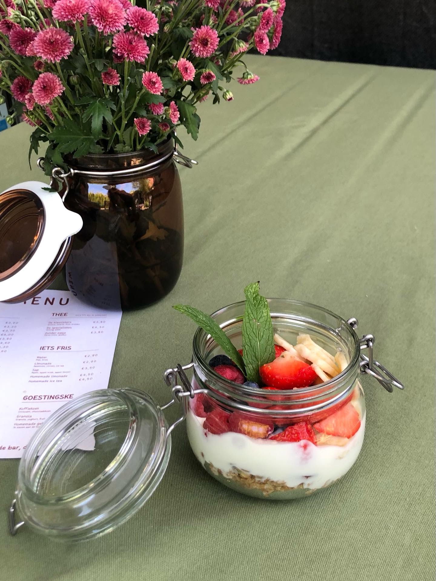 Yoghurtparfait met aardbeien, blauwe bessen en munt naast een vaasje roze bloemen